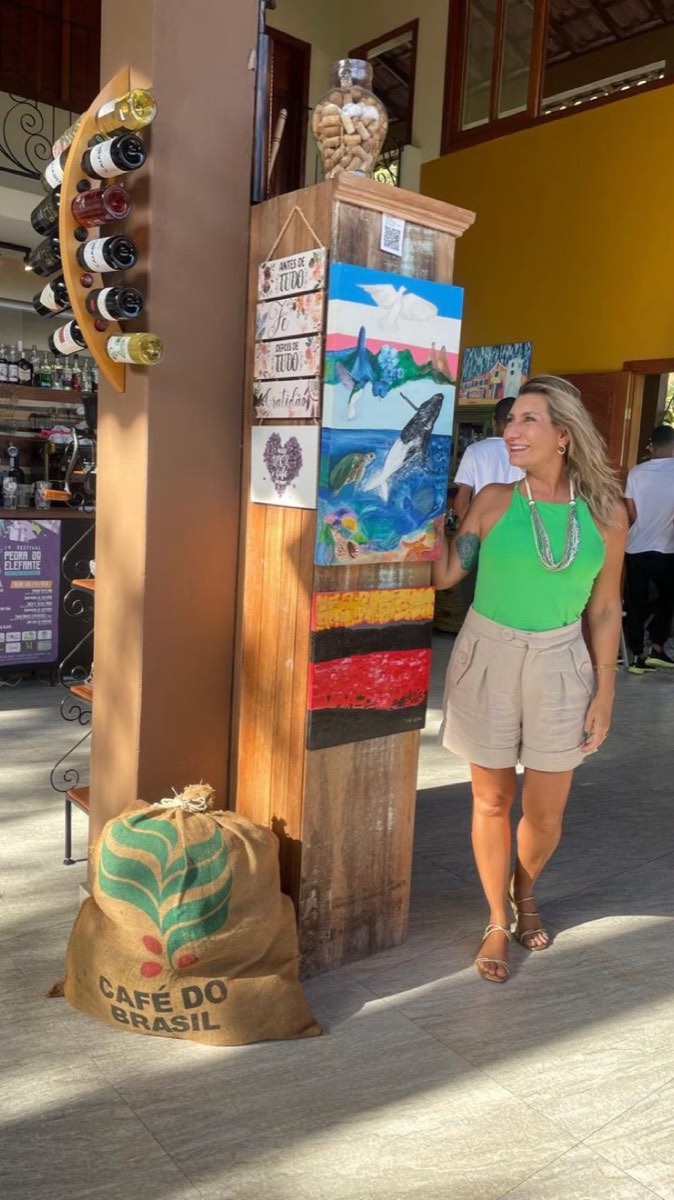 Cristine Aoni ao lado de obras expostas, com "Ícones Capixabas I" no alto