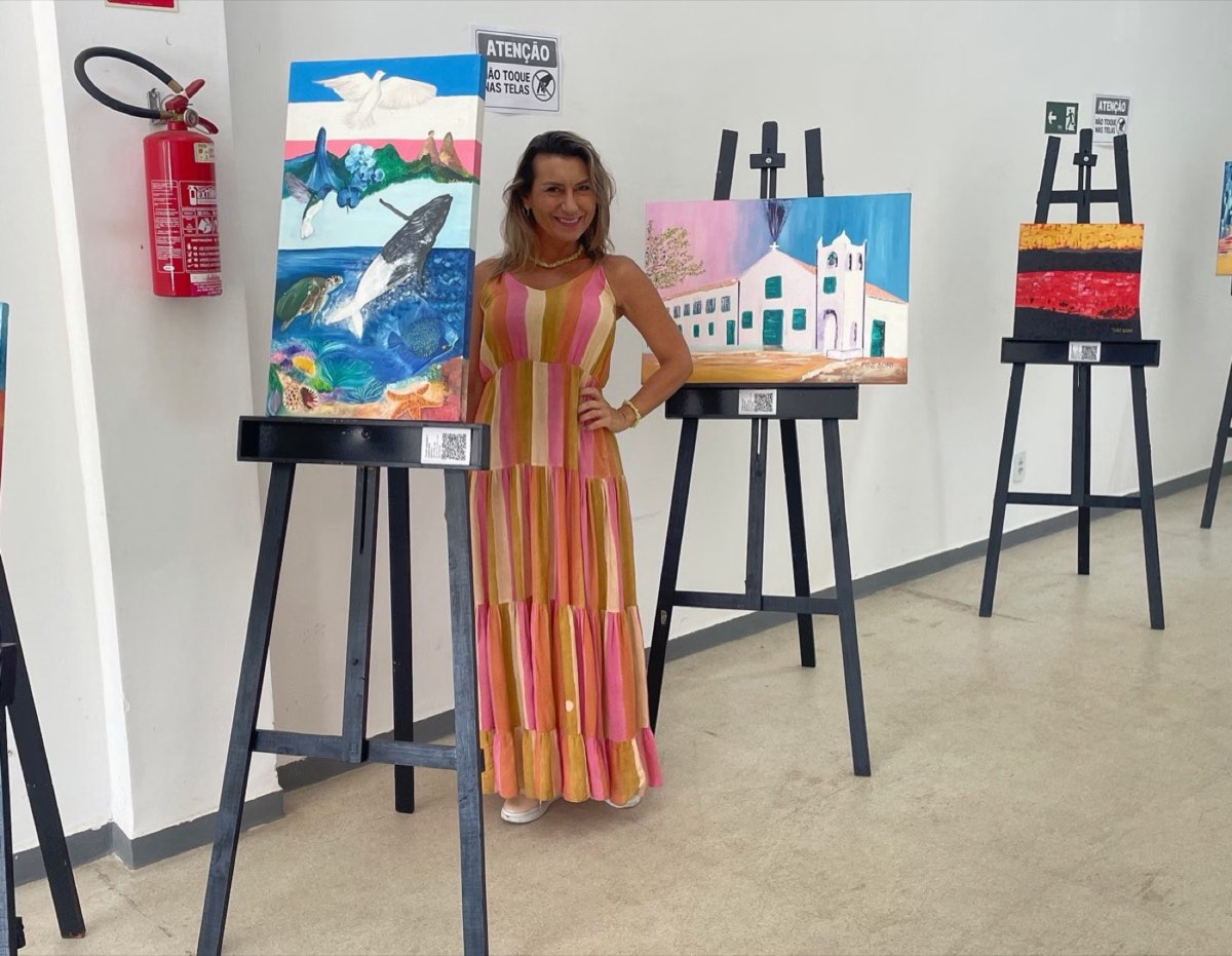 Cristine Aoni em uma exposição, entre telas em cavaletes