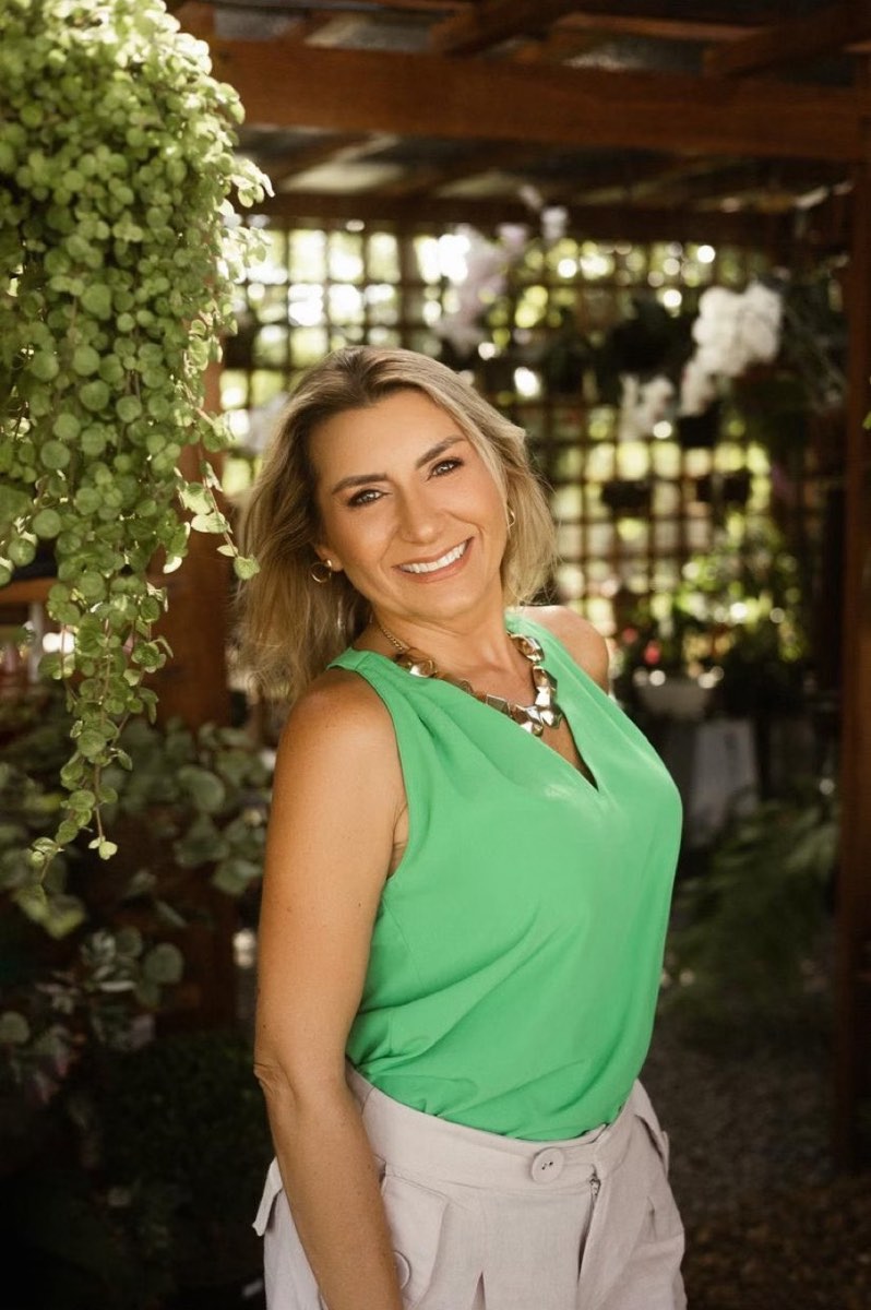 Cristine Aoni sorrindo, de blusa verde, entre plantas